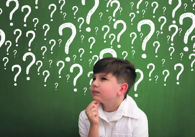 Elève devant tableau noir rempli de points d'interrogations © iStock