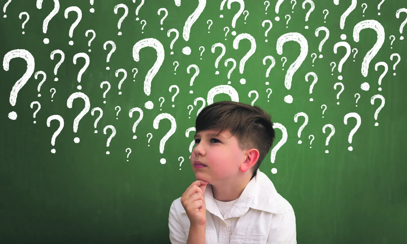 Elève devant tableau noir rempli de points d'interrogations © iStock