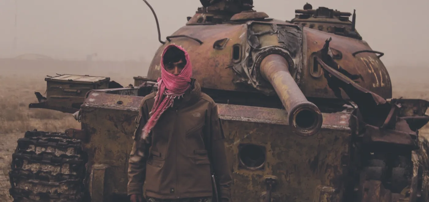 Août 2021, dans un faubourg de Kaboul (Afghanistan), un homme armé pose devant une épave de tank taliban. ©iStock/Trent Inness